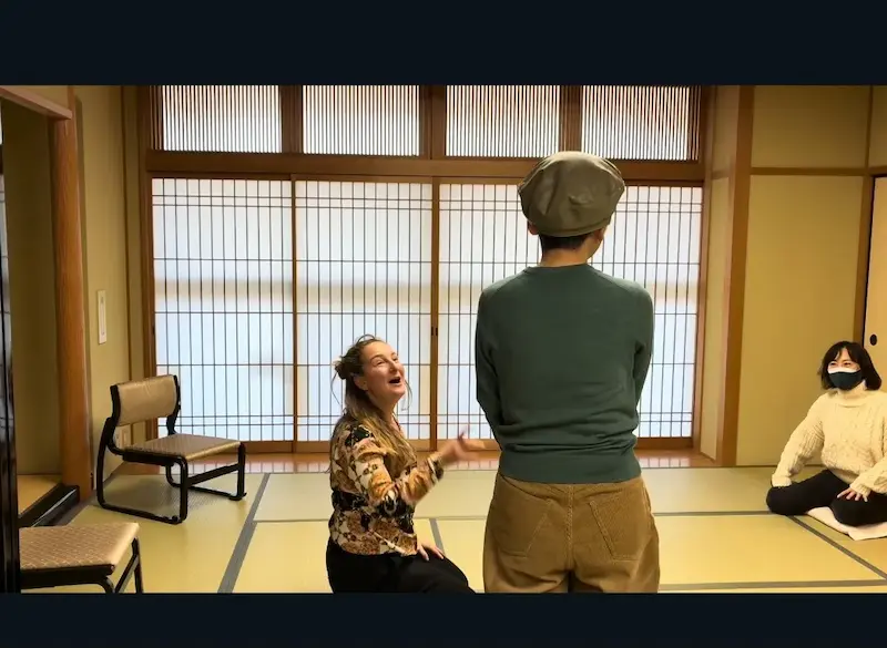 Oana leder en teaterbasert språkøkt i et japansk rom ved et kultursenter i Kyoto, mens to studenter improviserer og ler sammen.