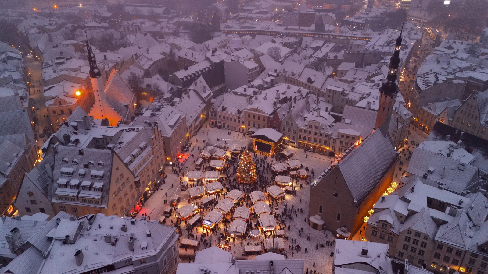 Julemarked i Europa: Rådhusplassen i Tallinn sett ovenfra, med snødekte tak, opplyste boder og juletre i skumringen