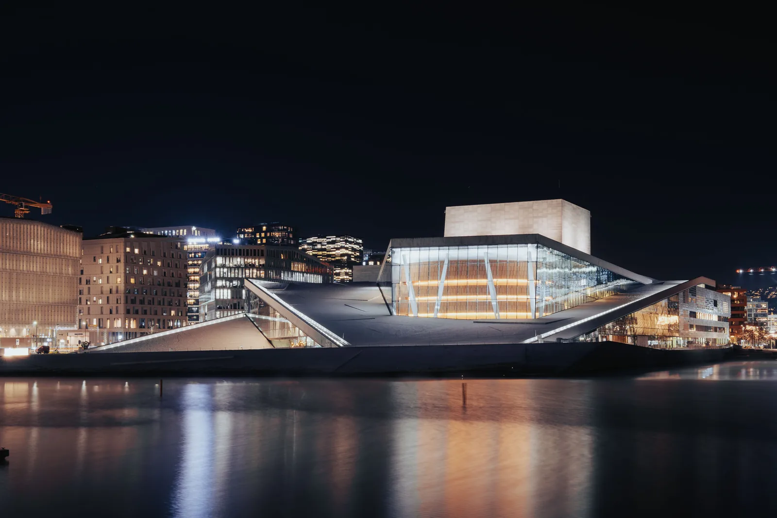 Konsert i Oslo: operahuset i Bjørvika opplyst om kvelden, med lysene speilet i vannet