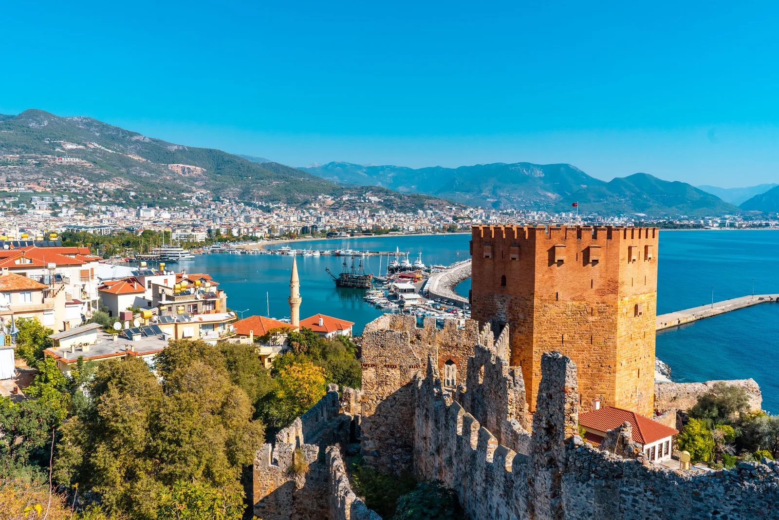 Det røde tårnet og havnen i Alanya med bymurene og fjellene bak