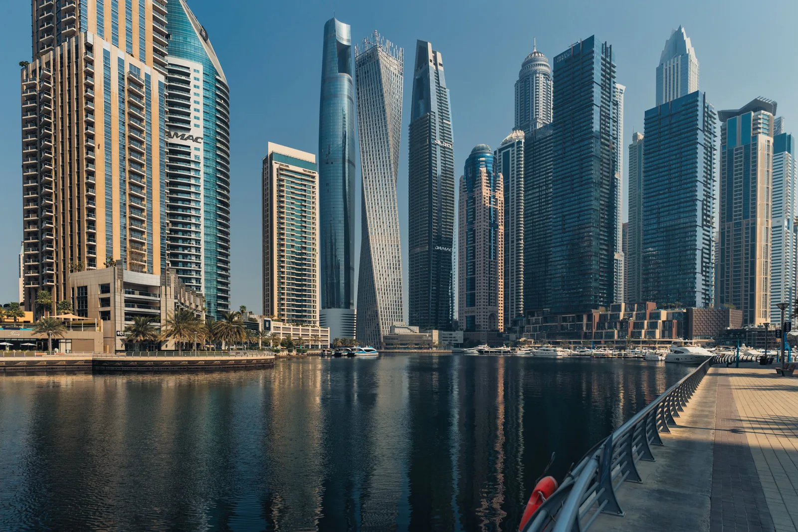 Skyskrapere langs kanalen i Dubai Marina en solrik dag, med en promenade ved vannkanten