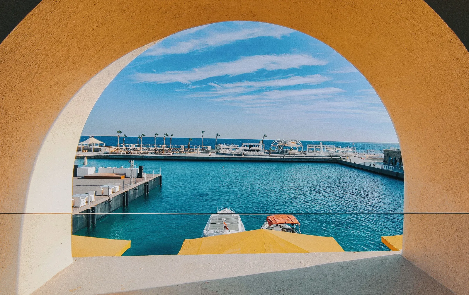 Marinaen i Hurghada sett gjennom en gul buegang, med turkist vann i Rødehavet og en båt ved kaien