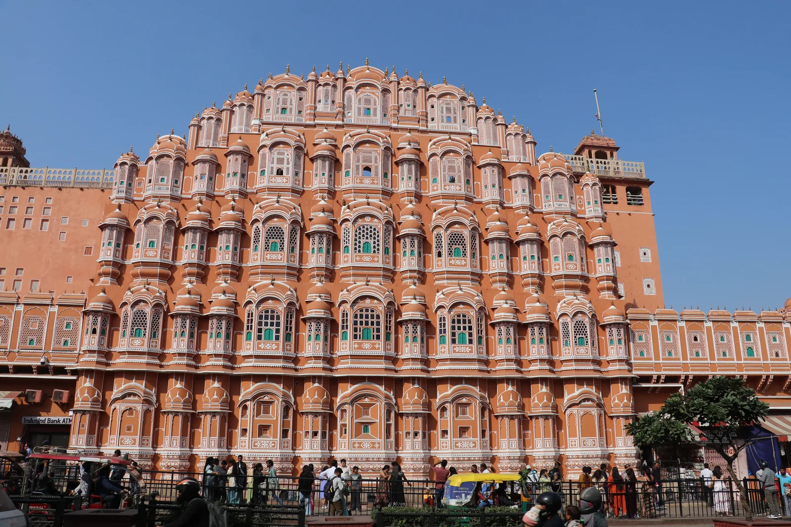 Hawa Mahal, vindpalasset i rosa sandstein, i Jaipur i Rajasthan i India, med folk og tuk-tuker i gaten foran