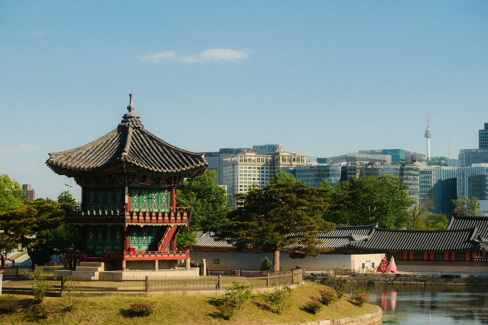 Tradisjonelt koreansk paviljongtak i et palassområde i Seoul, med moderne bygninger og Namsan-tårnet i bakgrunnen