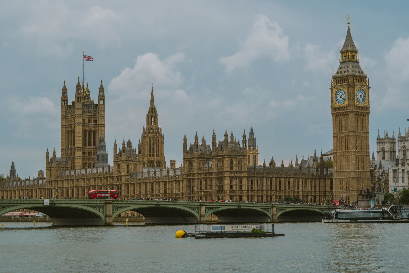 Big Ben og parlamentsbygningen i London sett fra Themsen, med Westminster Bridge og en rød buss på broen