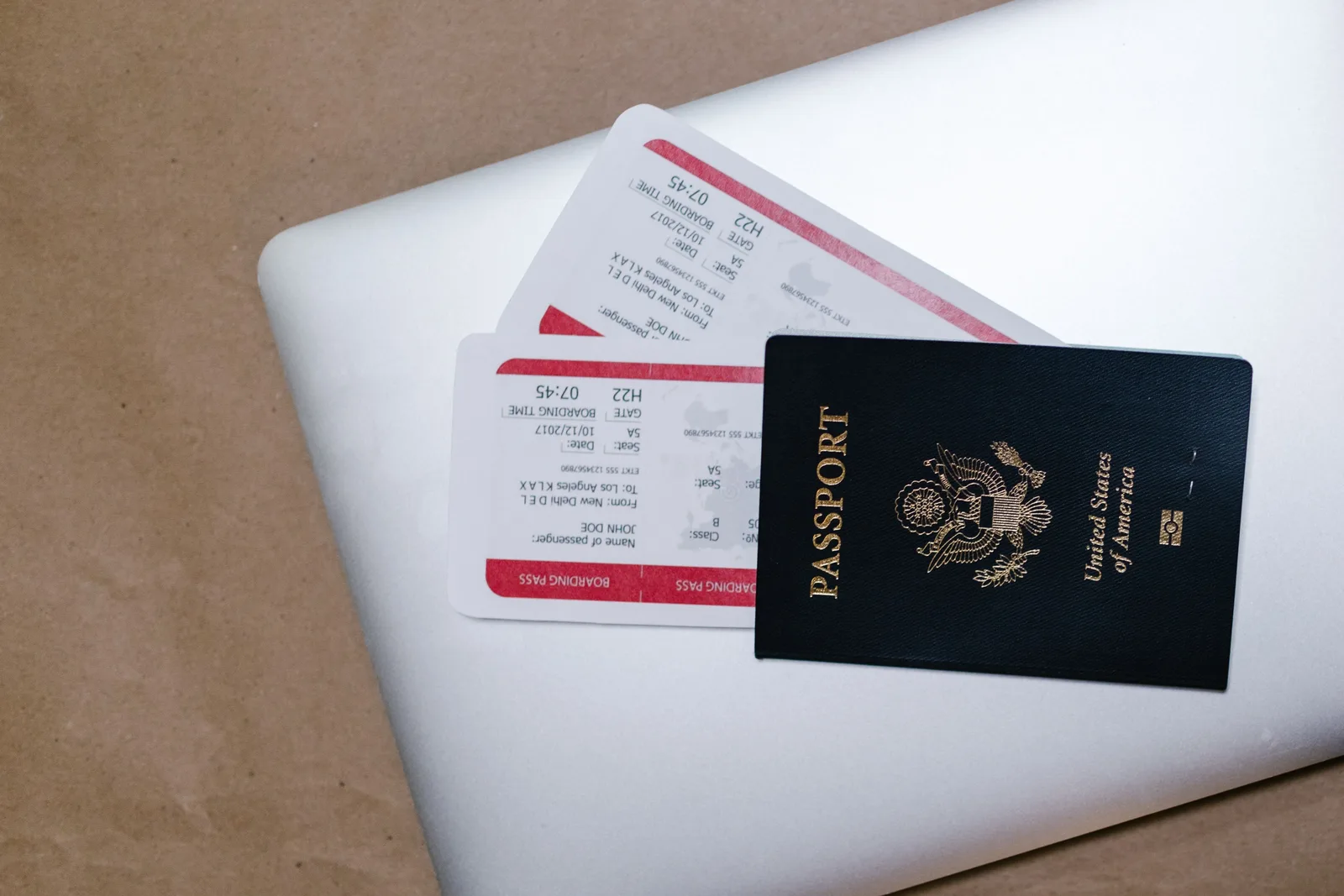 Amerikansk pass og to boardingkort ligger oppå en sølvfarget laptop på et brunt underlag