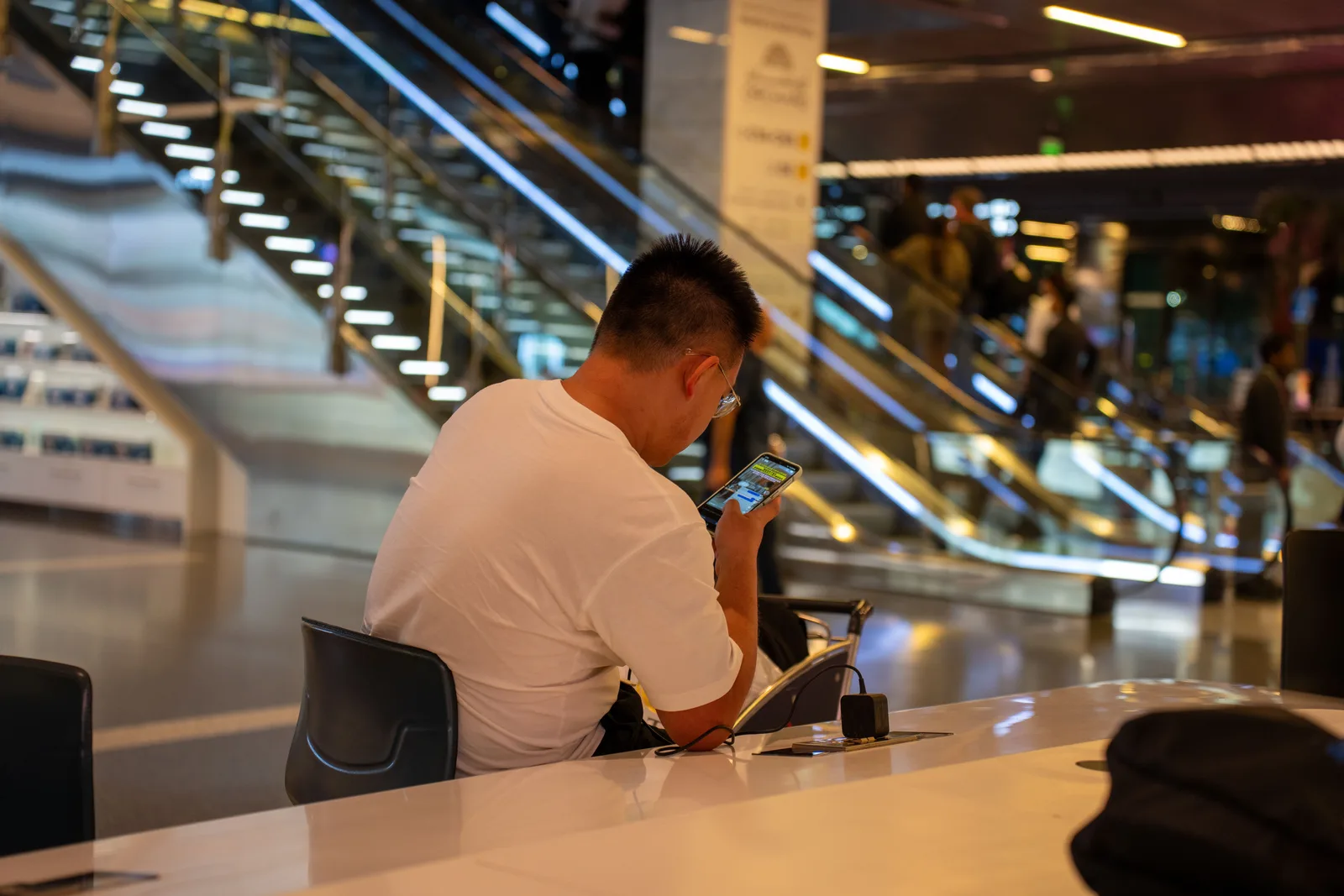 Mann sitter ved et bord i en flyplassterminal og ser på mobilen