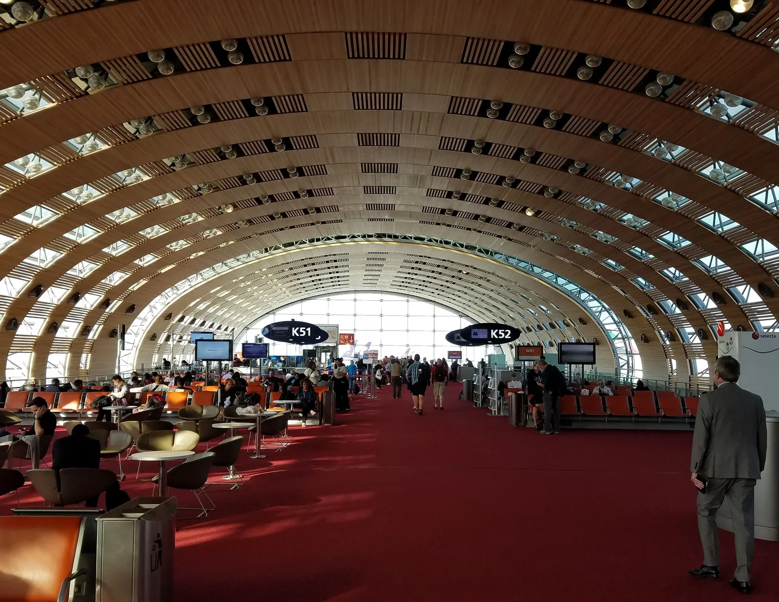 Ventehall i en terminal på Charles de Gaulle med buet trehvelv i taket og røde gulvtepper