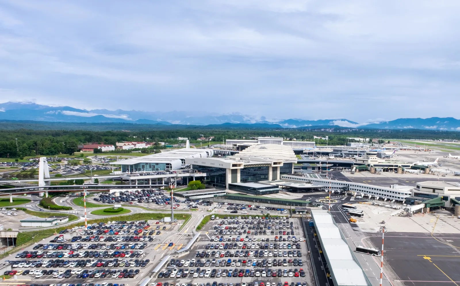 Flyfoto av terminalbygningene og parkeringsplassene på Milano Malpensa med fjell i bakgrunnen
