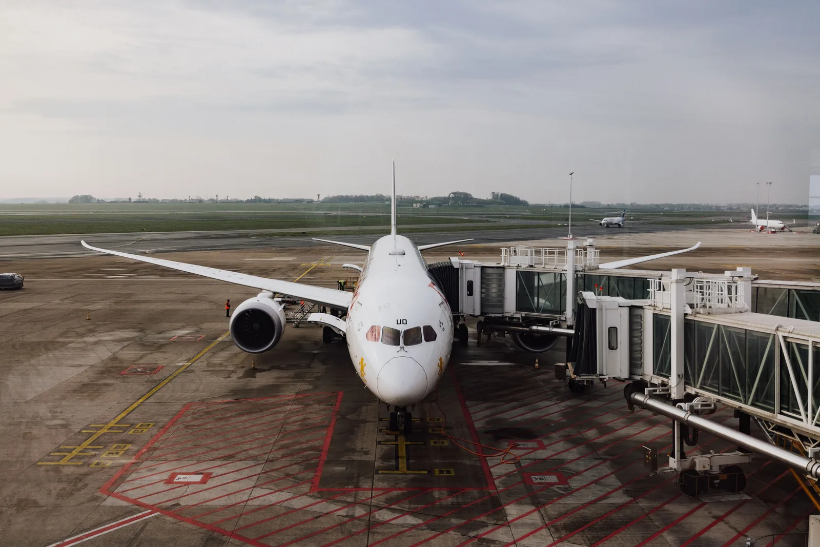 Et hvitt passasjerfly parkert ved en gate med to fingerbroer under en skyet himmel, med flere fly i bakgrunnen