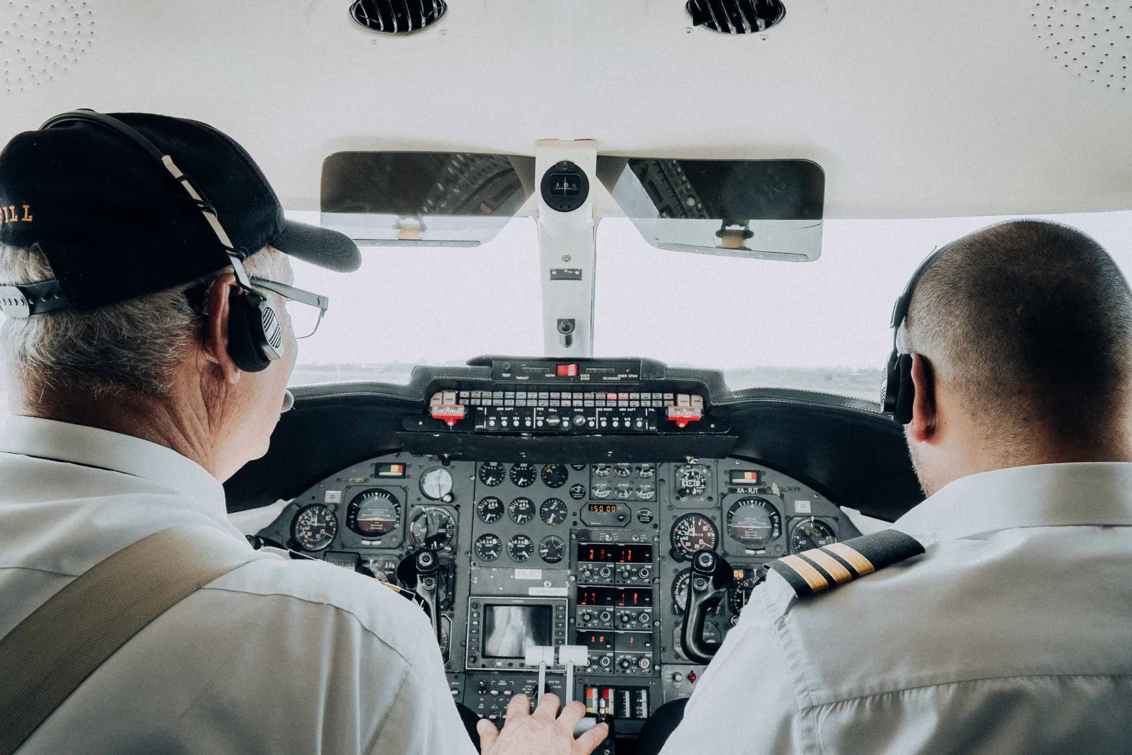 To piloter sett bakfra i cockpiten på et passasjerfly, den ene med caps og den andre i hvit uniformsskjorte med epåletter