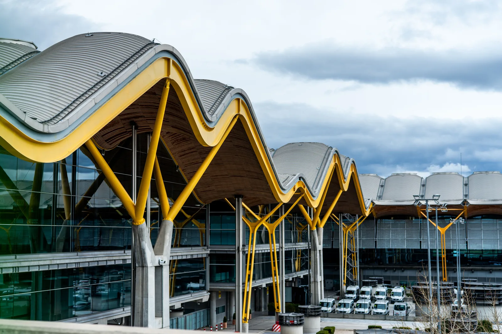 Taket og fasaden på terminalbygningen på Madrid-Barajas flyplass med bølgeformet tak i gult og hvitt under en delvis skyet himmel