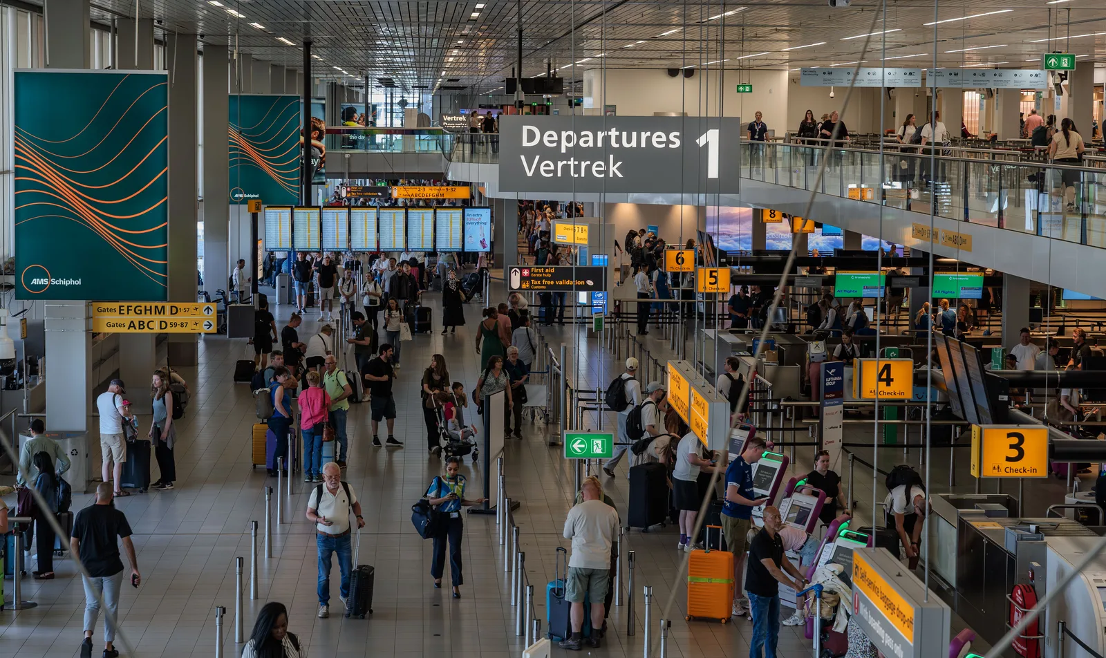 Avgangshallen på Amsterdam Schiphol med reisende i kø ved innsjekkingen og skilt for gate og avgang