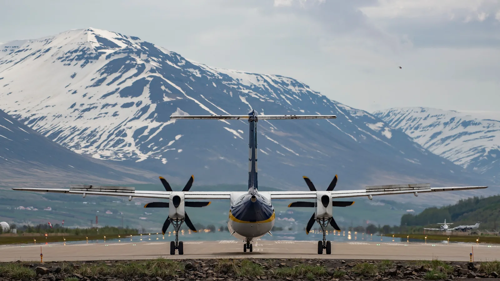 Propellfly av typen Dash 8 sett forfra på en rullebane med snødekte fjell i bakgrunnen