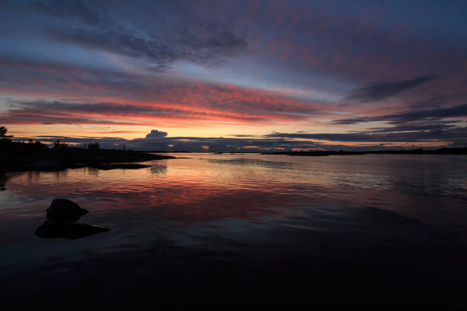 Solnedgang med rødt og blått lys over stille vann og svaberg i Hvaler-skjærgården