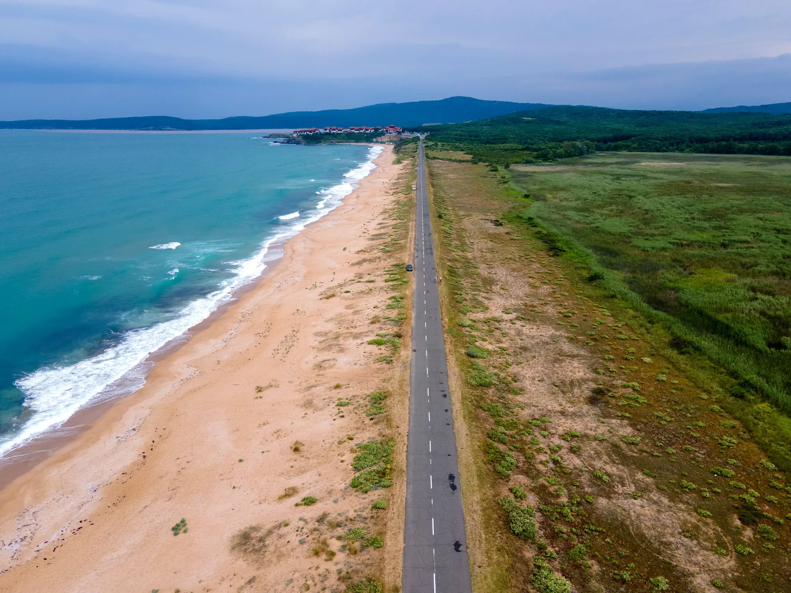 Smal vei langs en lang sandstrand ved Svartehavet i Bulgaria, sett ovenfra, med turkis sjø og grønt landskap