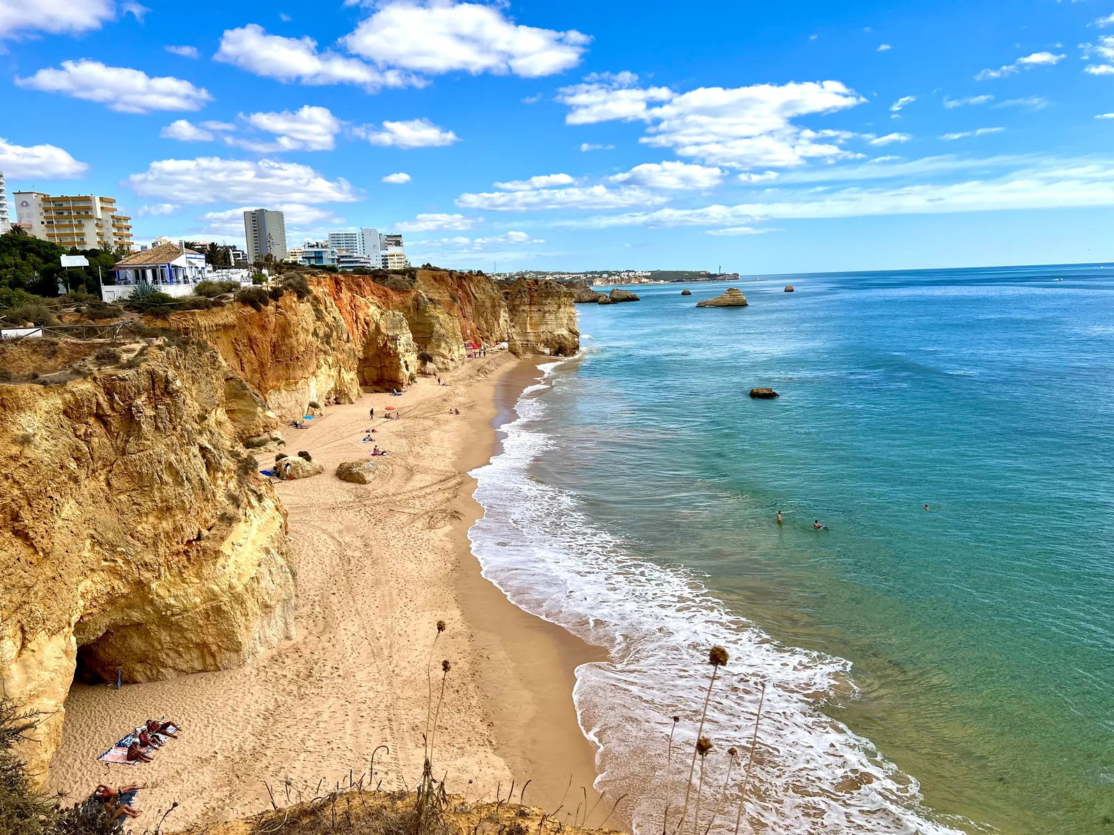 Oransje klipper, sandstrand og turkis sjø langs kysten av Algarve under blå himmel