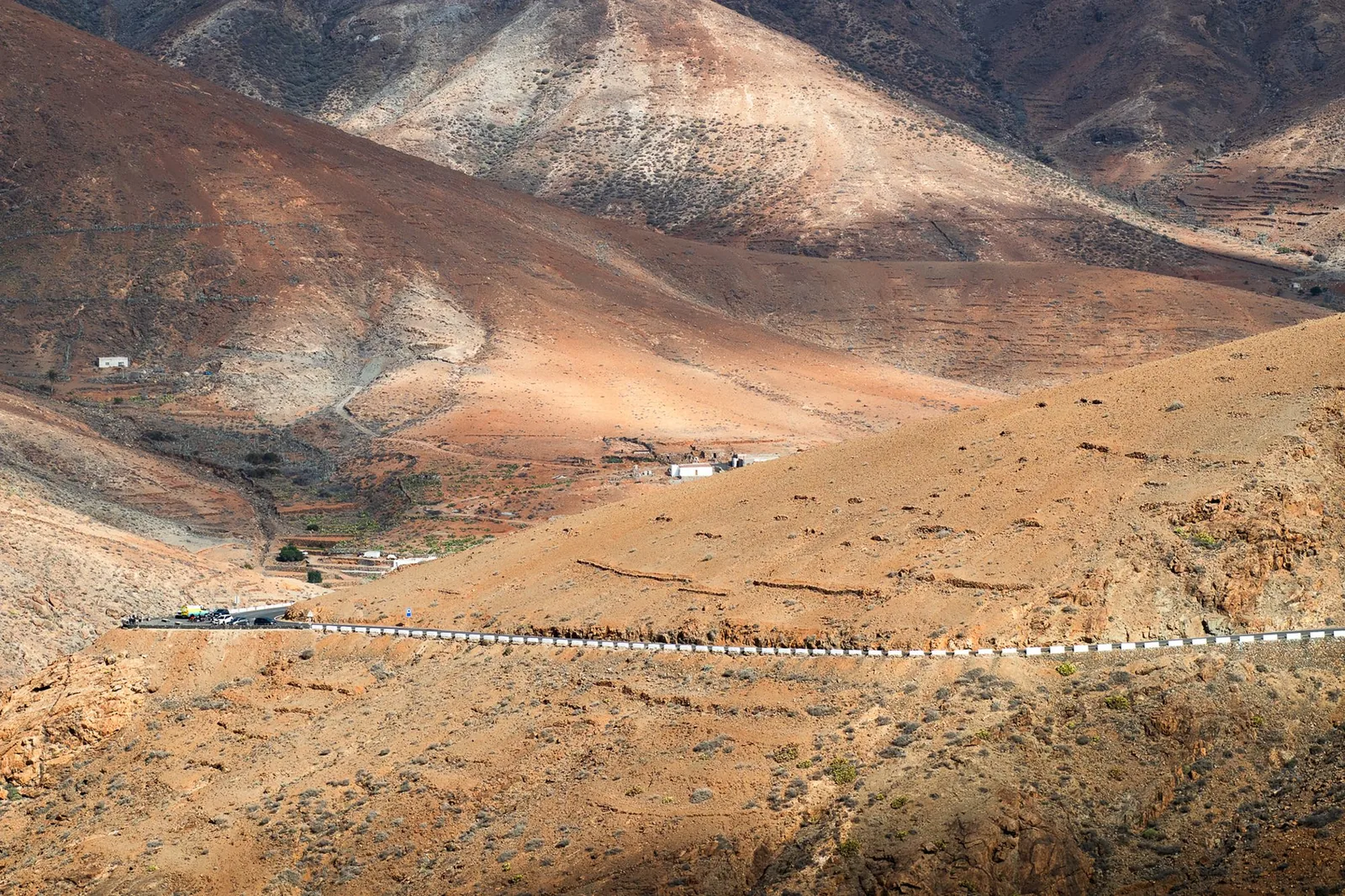 Asfaltert vei som svinger gjennom brunt fjellandskap på Fuerteventura