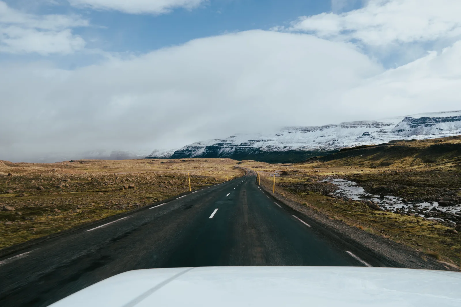 Asfaltert vei på Island som går mot snødekte fjell under en lys himmel