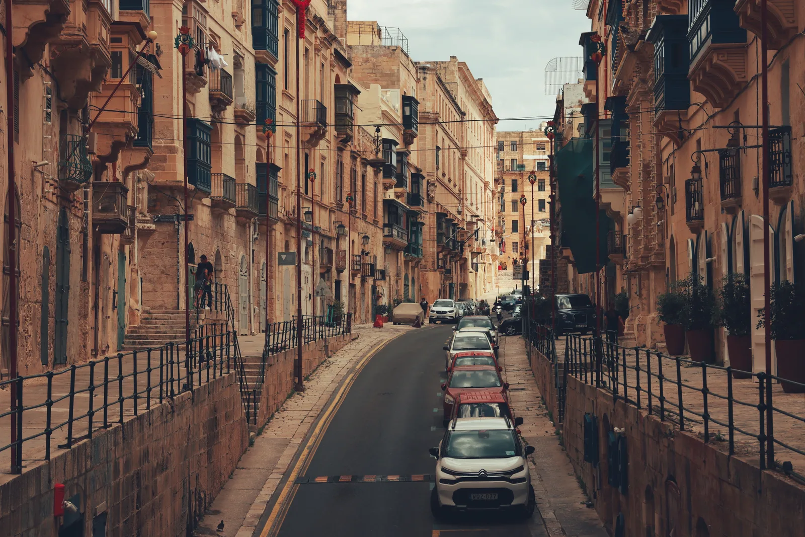 Smal gate med gamle kalksteinsbygninger og balkonger i Valletta på Malta, med en liten hvit bil på vei oppover