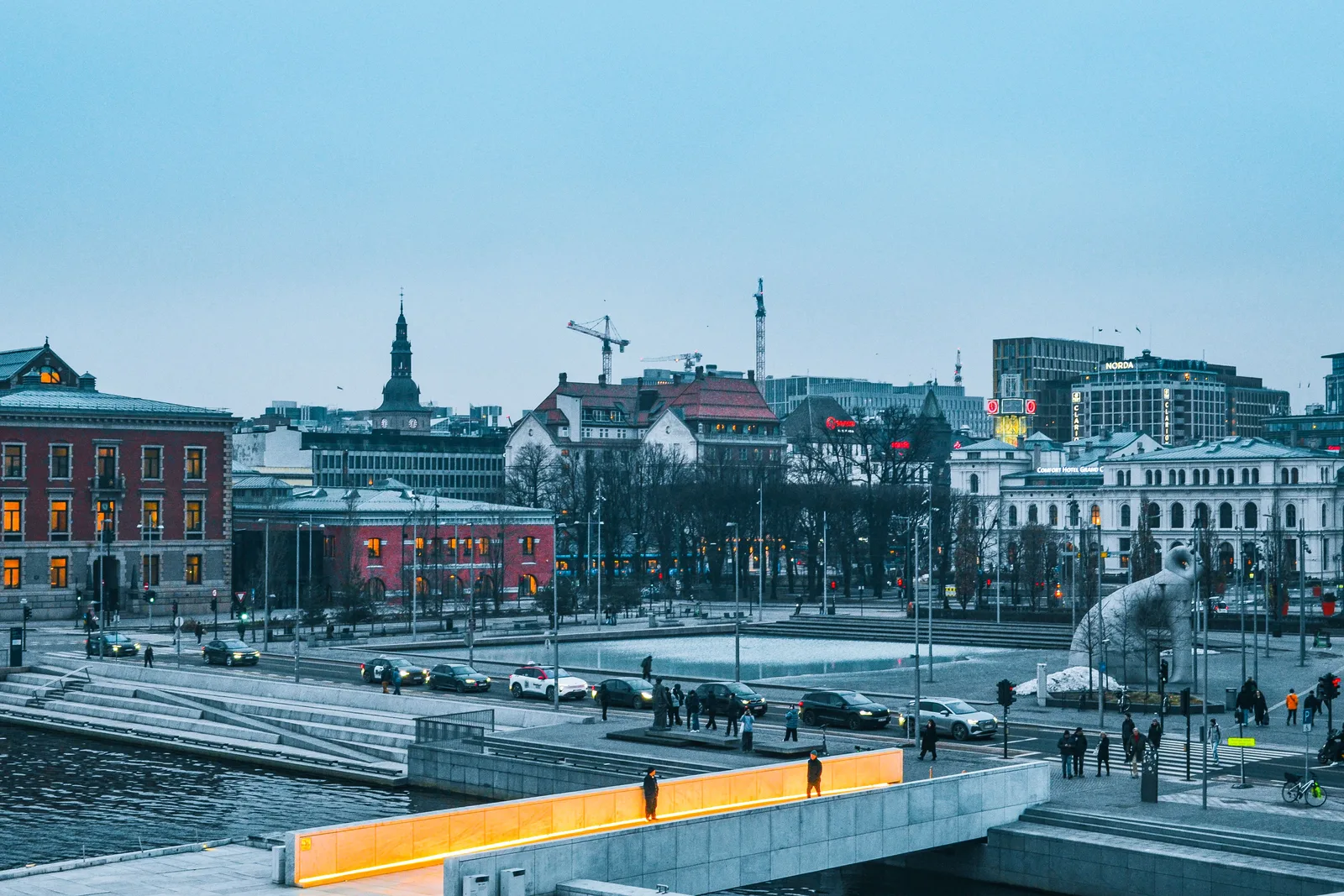 Gate i Oslo sentrum ved havnen med biler, kontorbygg og folk som går, sett i skumringen