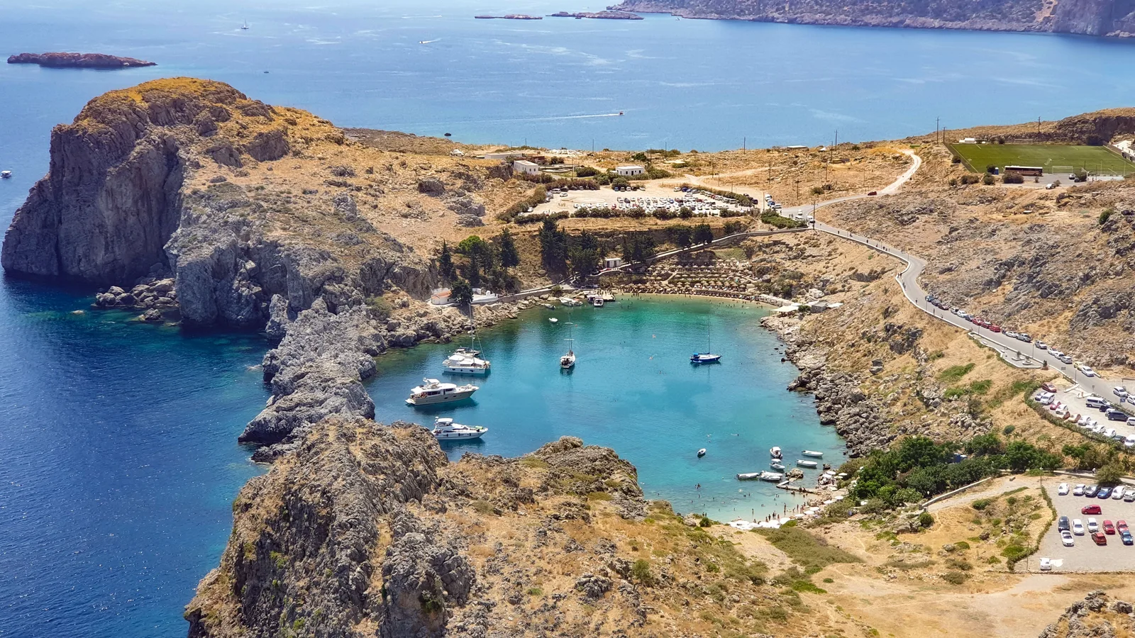 Utsikt over Sankt Pauls bukt ved Lindos på Rhodos med turkis sjø, klipper og en vei som går langs kysten