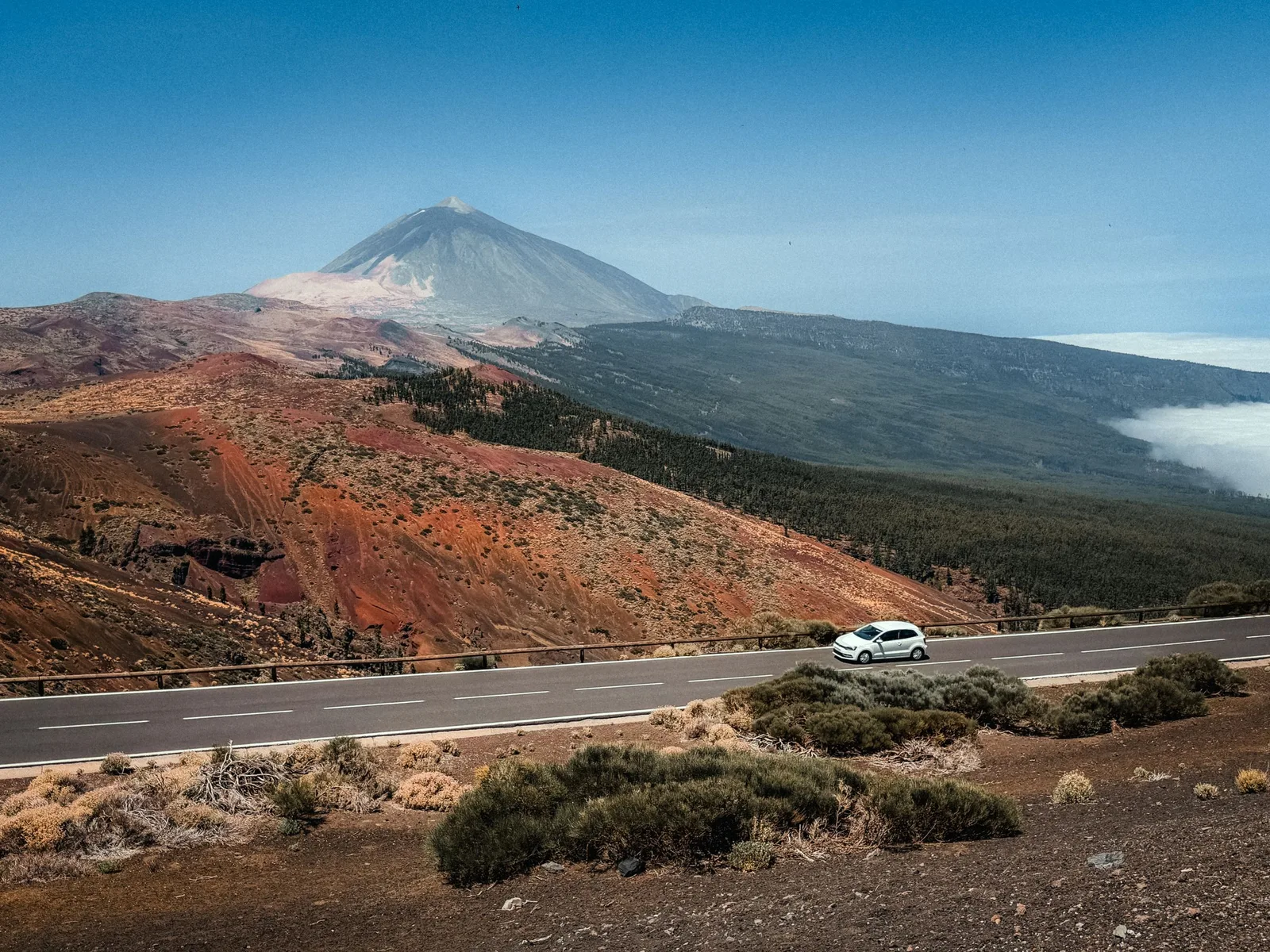 En hvit bil kjører på veien i Teide nasjonalpark på Tenerife, med vulkanen Teide i bakgrunnen
