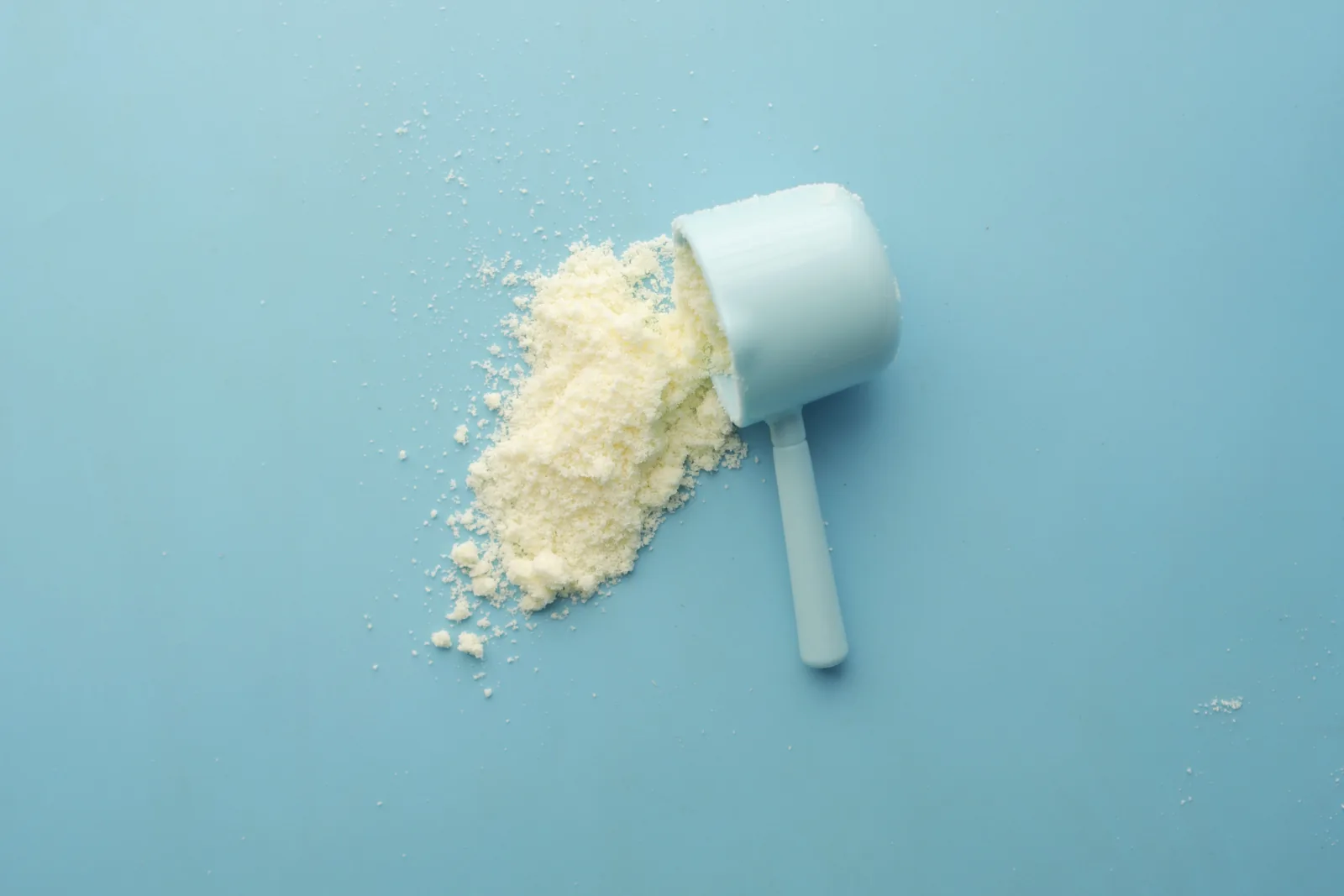 Ljust proteinpulver som hälls ut ur en vit mätsked mot en blå bakgrund