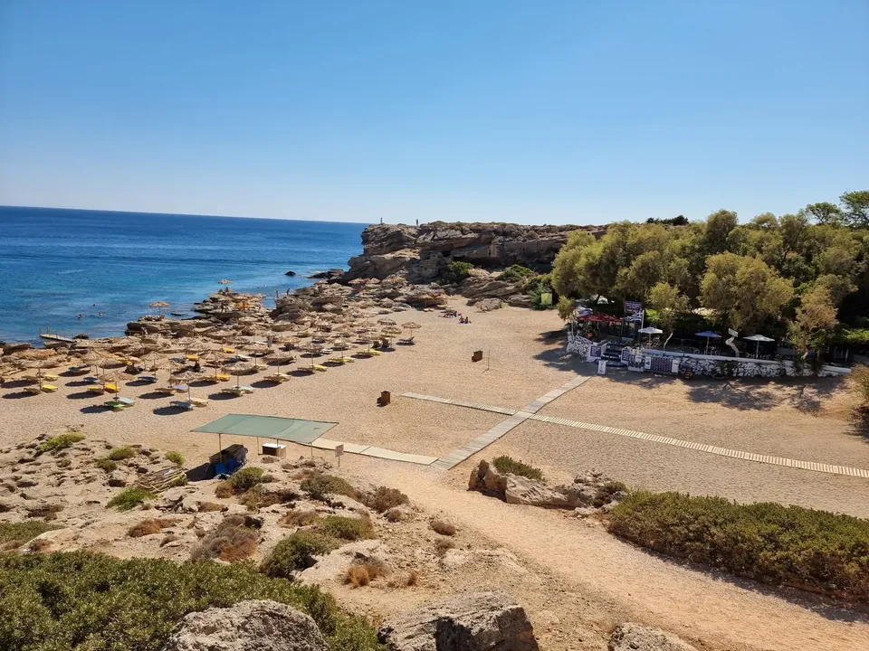 Rolig strand med parasoller og busker ved klart vann på Rhodos