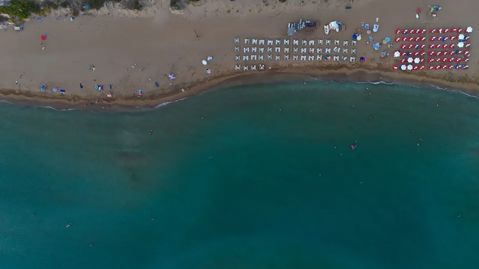 Sandstrand med rader av parasoller og solsenger ved turkist hav, sett ovenfra