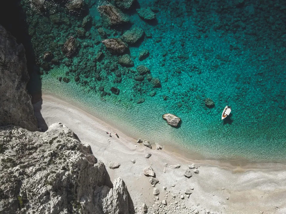 Liten sandstrand mellom hvite klipper og turkist vann, sett ovenfra