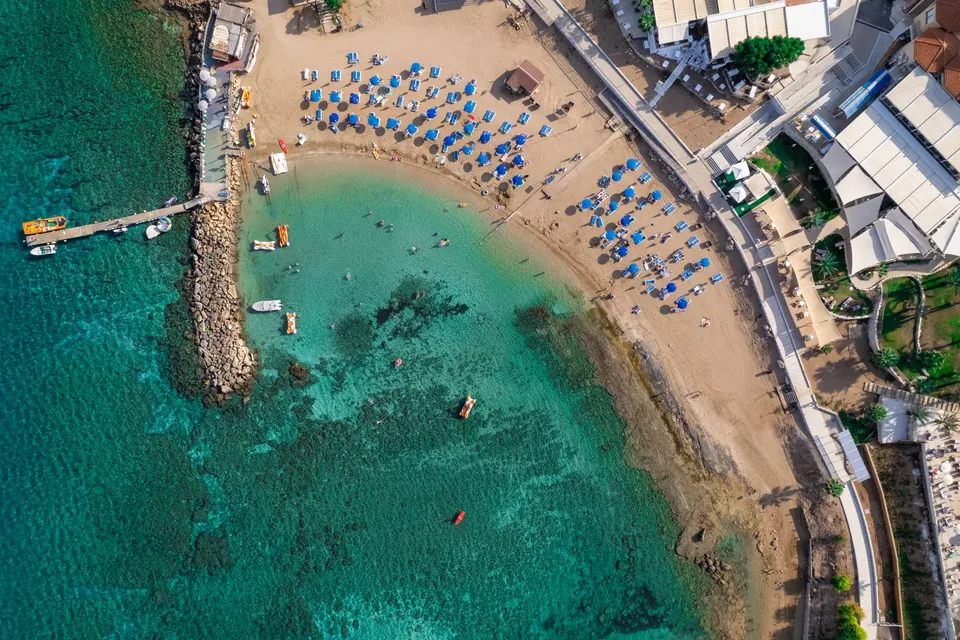 Turkis bukt med sandstrand, parasoller og en brygge ved Protaras sett ovenfra