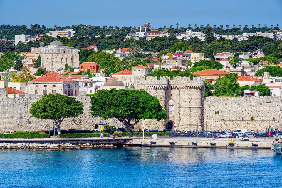 Bymuren og havnen i Rhodos by med trær og hus bak muren