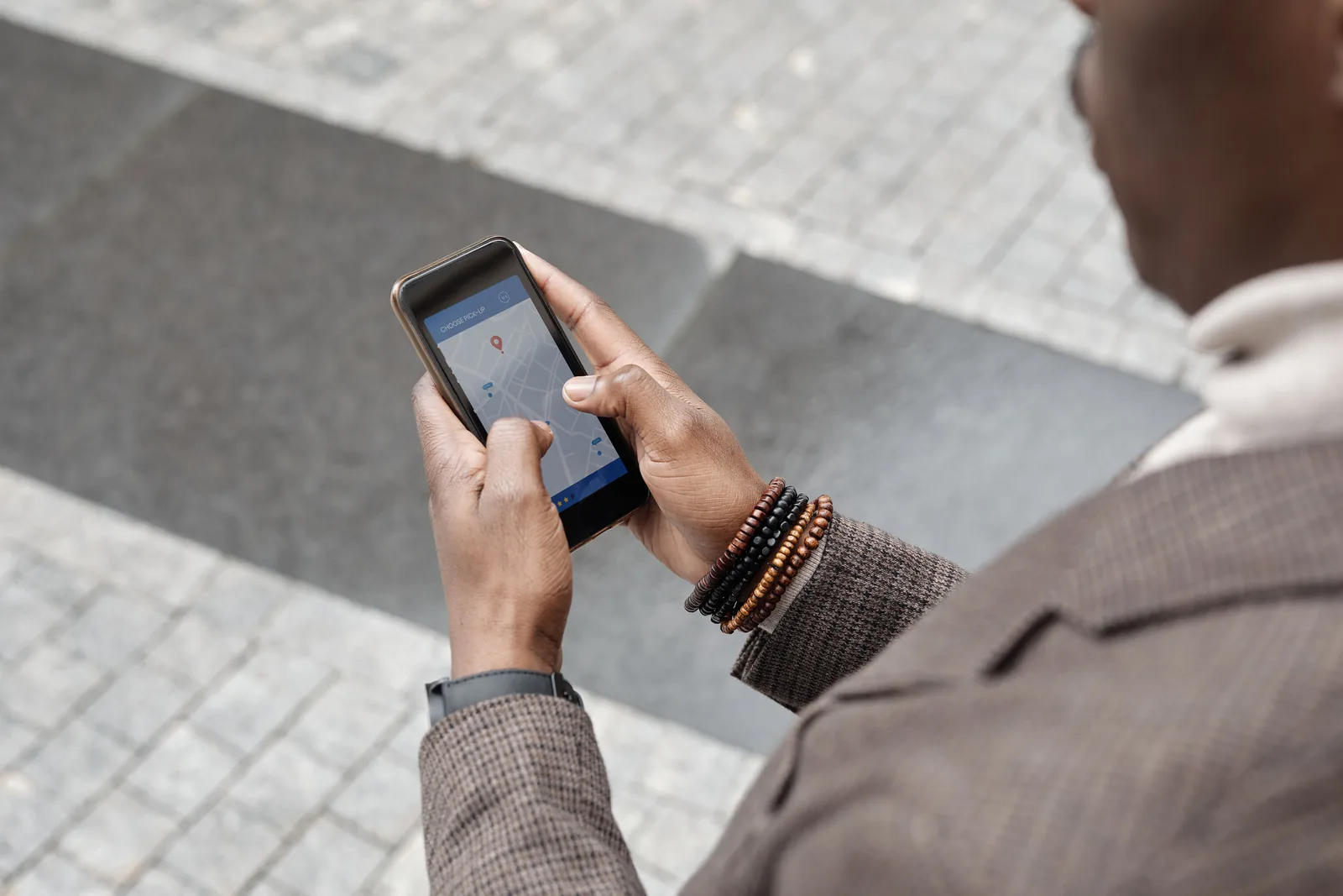 Mann i tweedjakke holder en mobiltelefon med kartapp åpen på et fortau i en by