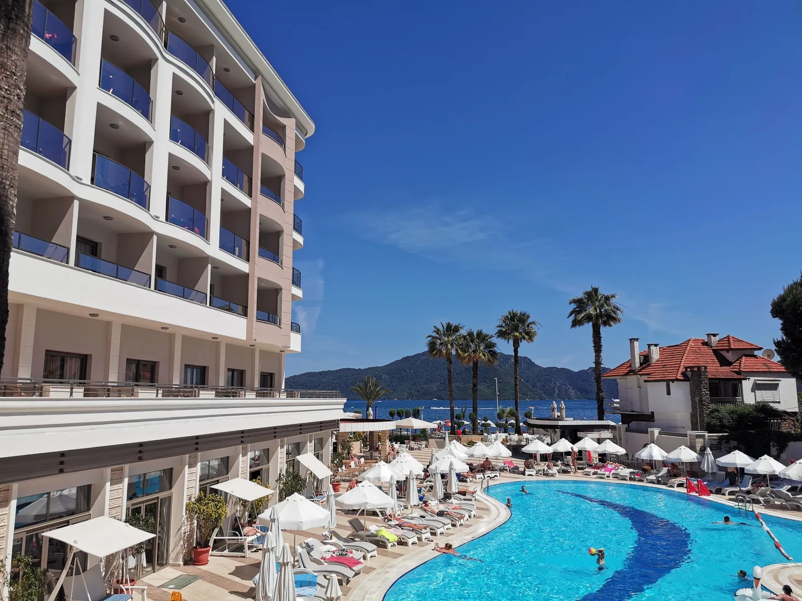Hotell med balkonger ved et basseng i Marmaris med solsenger, parasoller og palmer